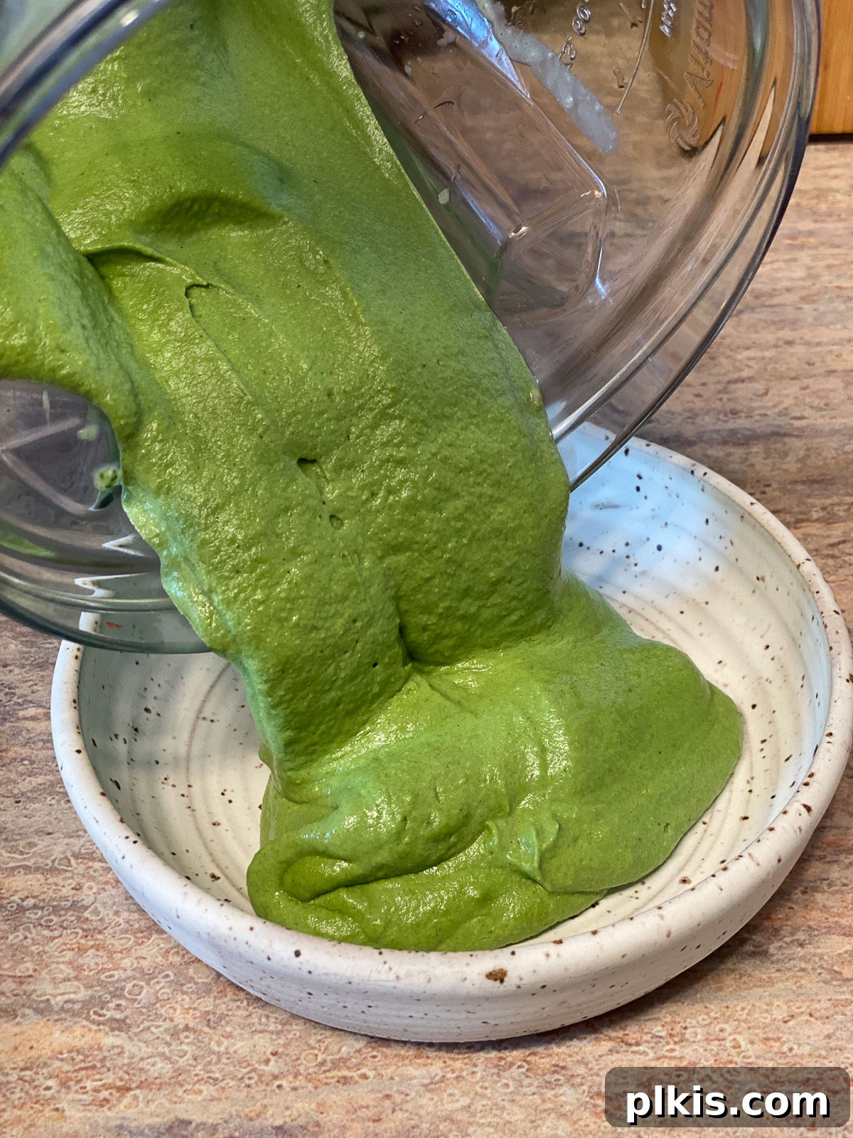 Dreamy Vegan Spinach Dip 12 A smooth, vibrant green vegan spinach dip being poured from a blender into an elegant serving bowl, ready to be chilled and enjoyed with crackers and vegetables.