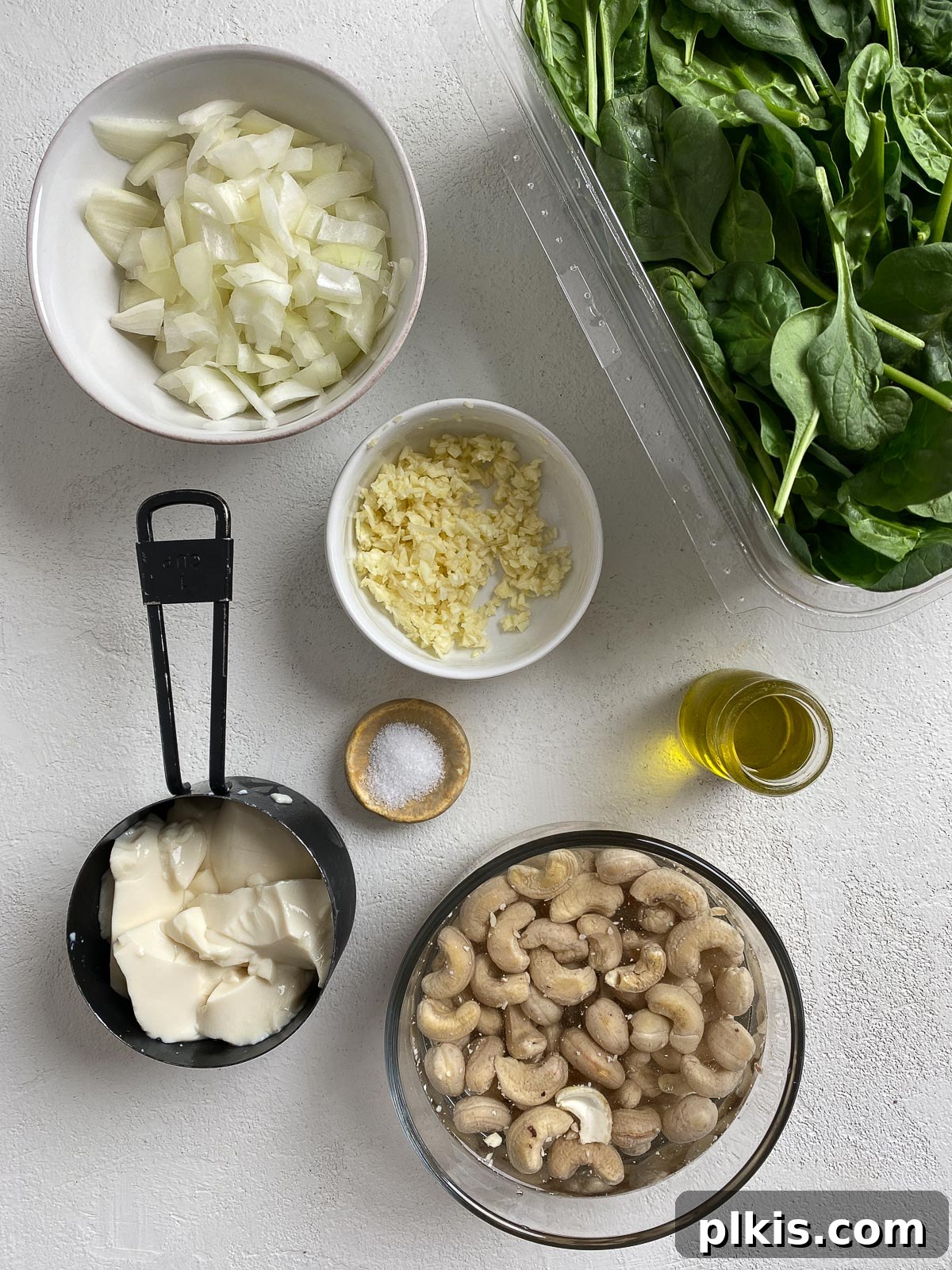 Dreamy Vegan Spinach Dip 3 A vibrant flat lay of fresh ingredients for vegan spinach dip, including bright green spinach, creamy cashews, a block of silken tofu, and aromatic garlic and onion, all arranged on a pristine white surface, ready for preparation.