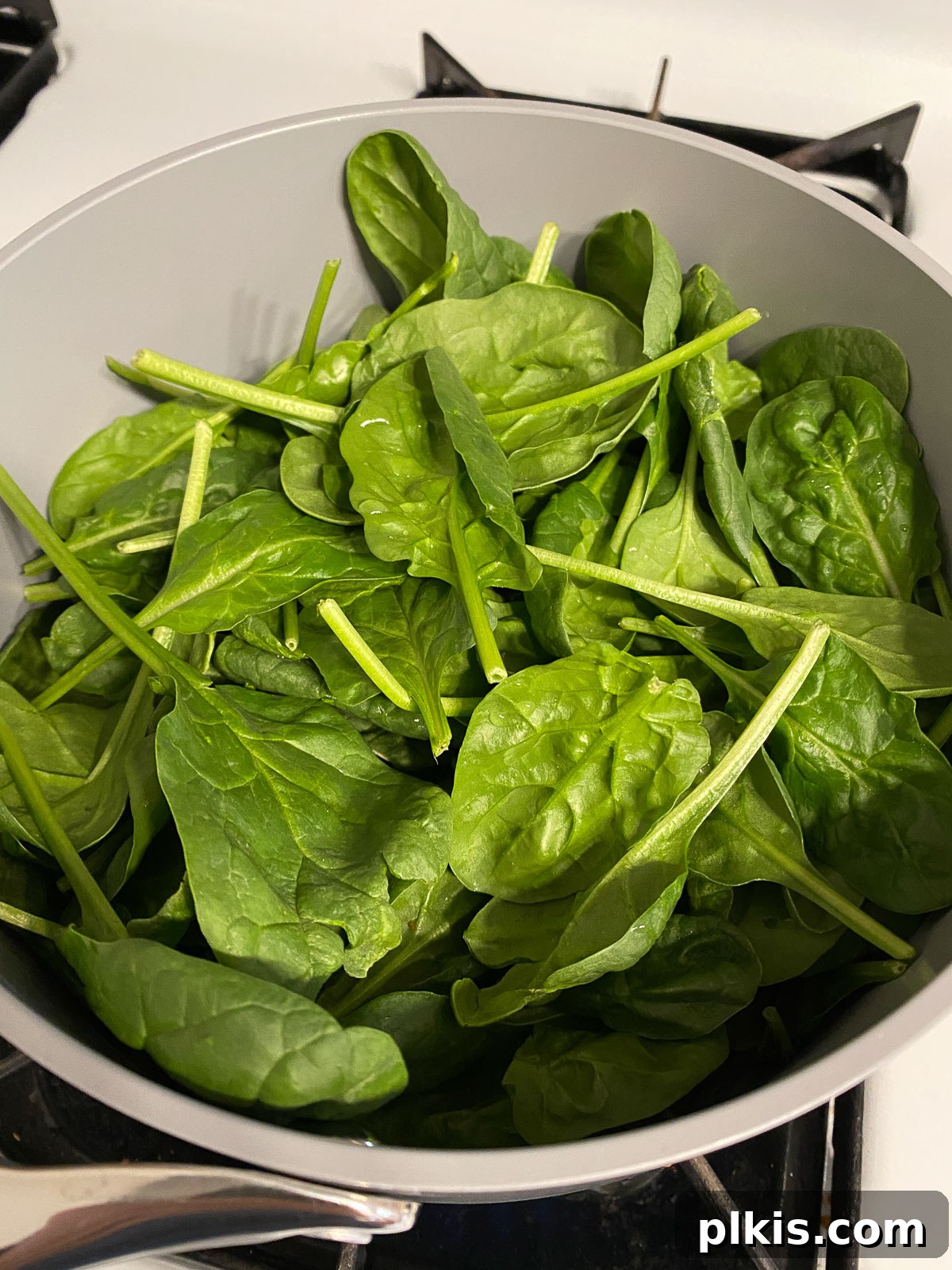 Dreamy Vegan Spinach Dip 4 A generous pile of vibrant raw spinach resting in a gray non-stick pan, ready to be wilted, with a hint of water visible at the bottom.