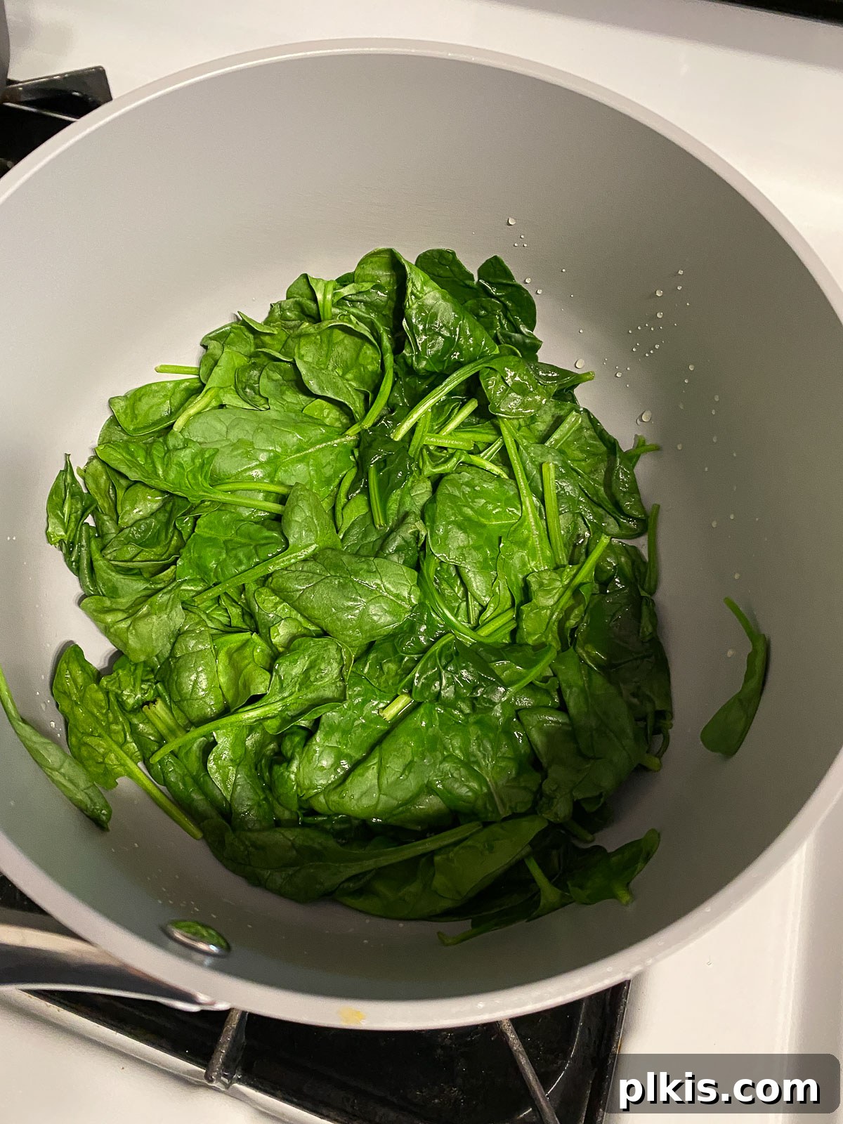 Dreamy Vegan Spinach Dip 5 Mid-process shot showing fresh spinach beginning to wilt in a pan, turning darker green and softening as it cooks down, preparing it for the creamy dip base.