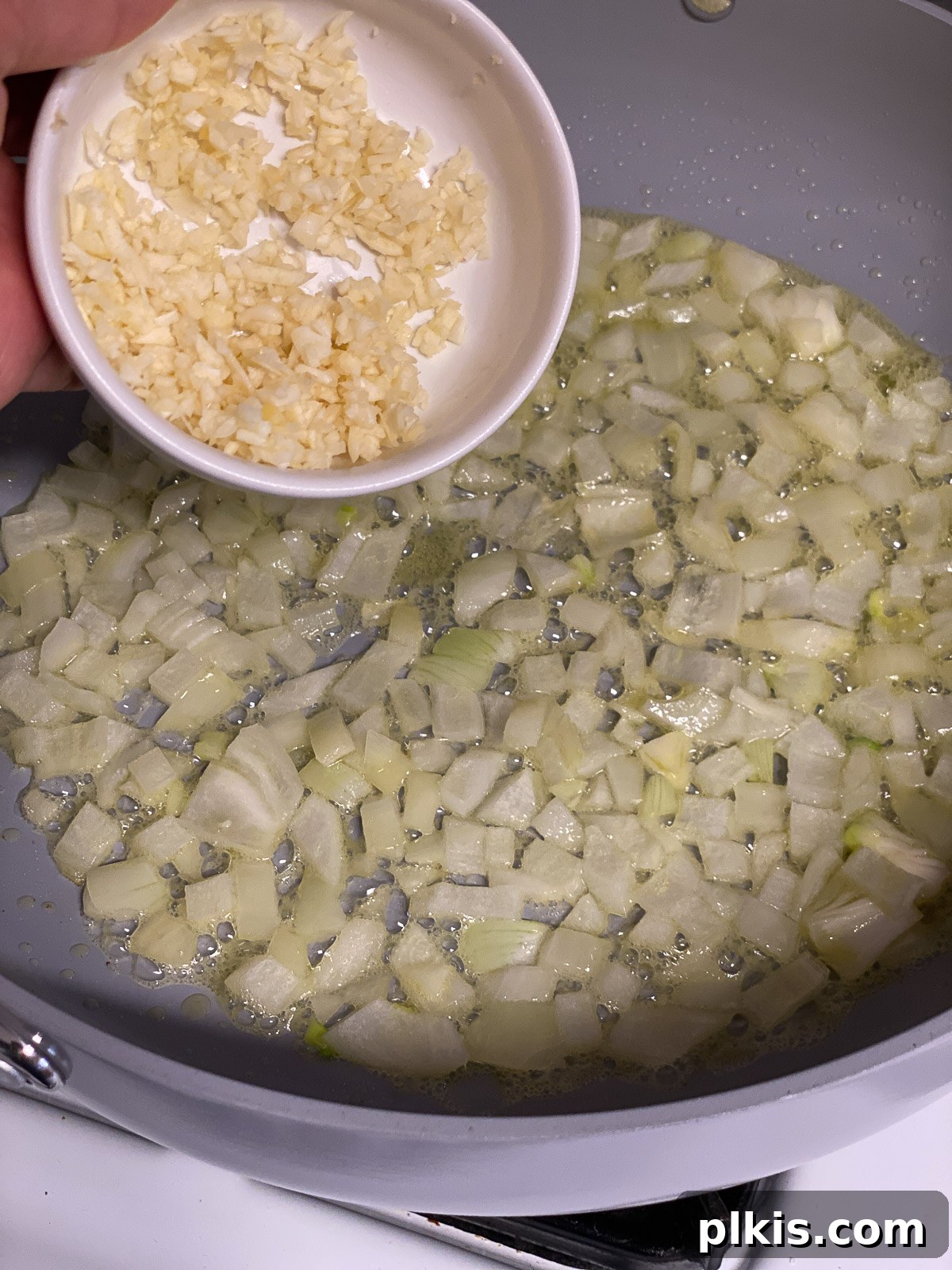 Dreamy Vegan Spinach Dip 7 Finely minced garlic cloves being added to the sautéing onions in a pan, releasing their aromatic fragrance to enhance the spinach dip base.