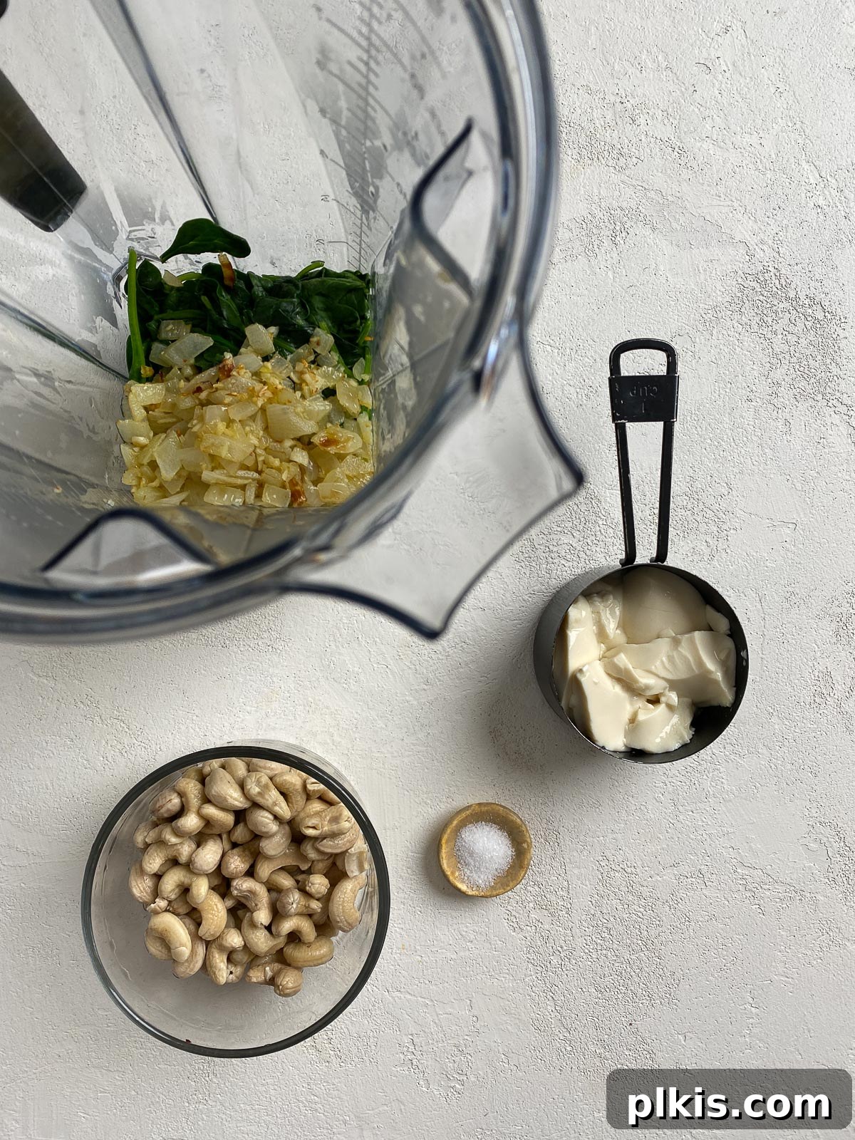 Dreamy Vegan Spinach Dip 9 All the fresh ingredients for the vegan spinach dip, including wilted spinach, cashews, tofu, and sautéed aromatics, laid out on a white counter next to a high-speed blender, ready for blending.