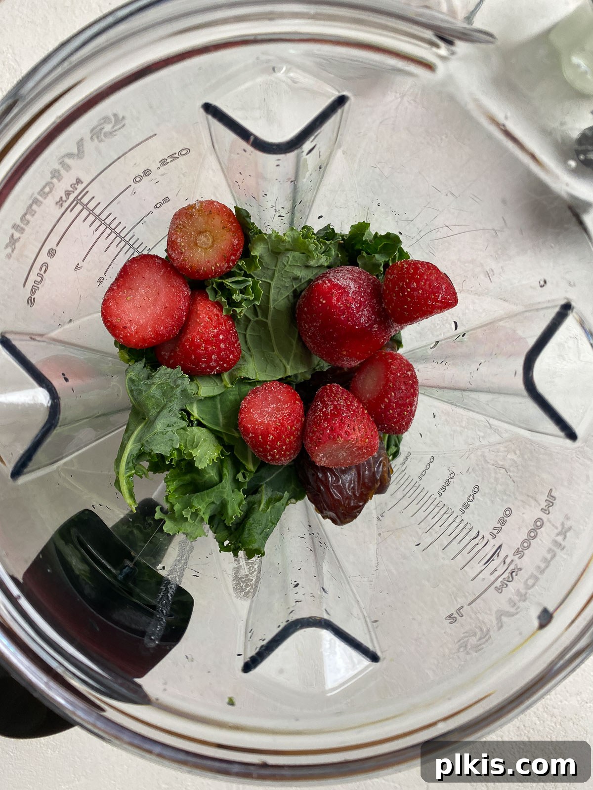 Strawberry Kale Power Elixir 4 Fresh strawberries, green kale leaves, a banana, and seeds visible in a blender jar, prepared for blending into a smoothie.