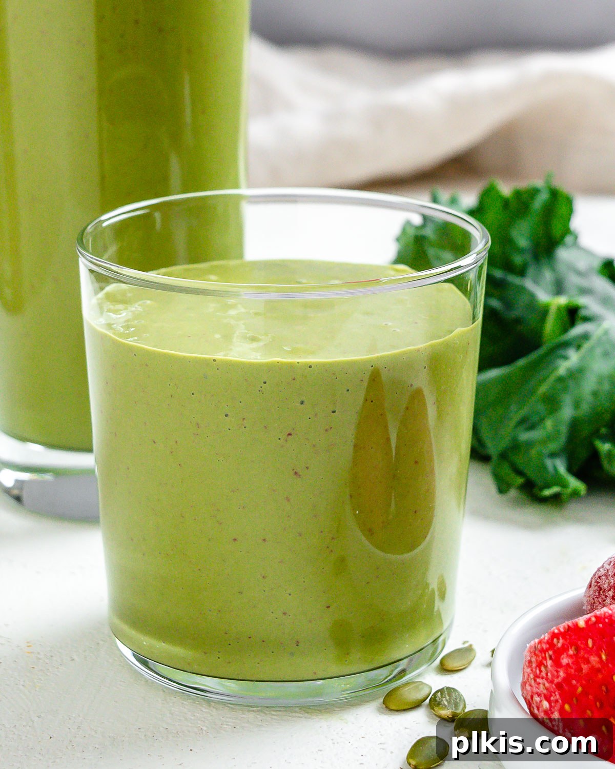 Strawberry Kale Power Elixir 5 Two beautiful glasses of Strawberry Kale Smoothie, perfectly blended and ready to drink, with fresh kale and strawberries decoratively arranged in the background.