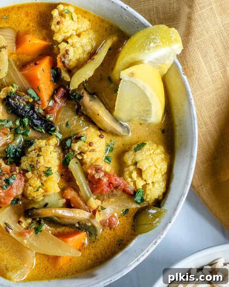 Golden Yam & Earthy Mushroom Curry with Cauliflower 5 A vibrant bowl of Cauliflower Sweet Potato Mushroom Curry, presented beautifully against a white background, with a subtle backdrop of fresh ingredients suggesting its wholesome nature.