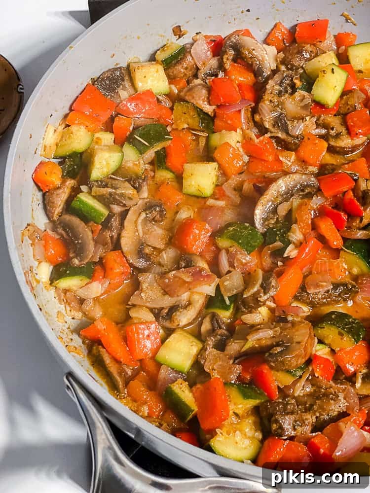 Process shot showing sliced mushrooms added to the pan with sauteed vegetables, ready to be seasoned and cooked further