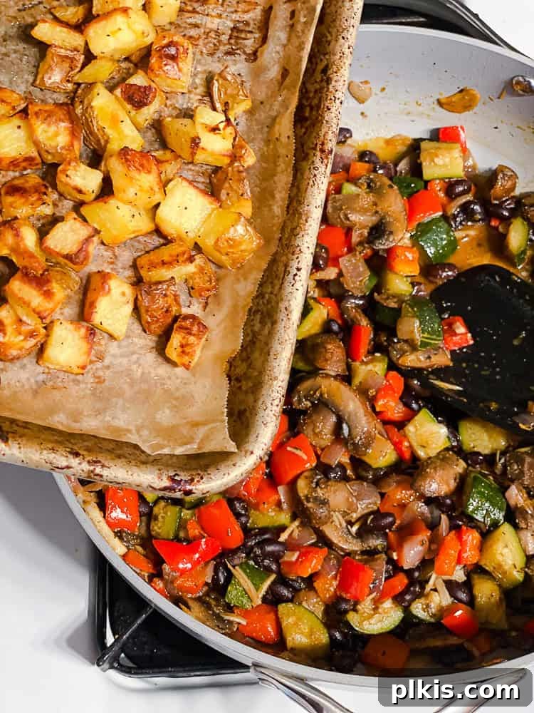 Process shot showing the roasted potatoes being added to the skillet with the cooked vegetable and bean mixture, ready for final combining