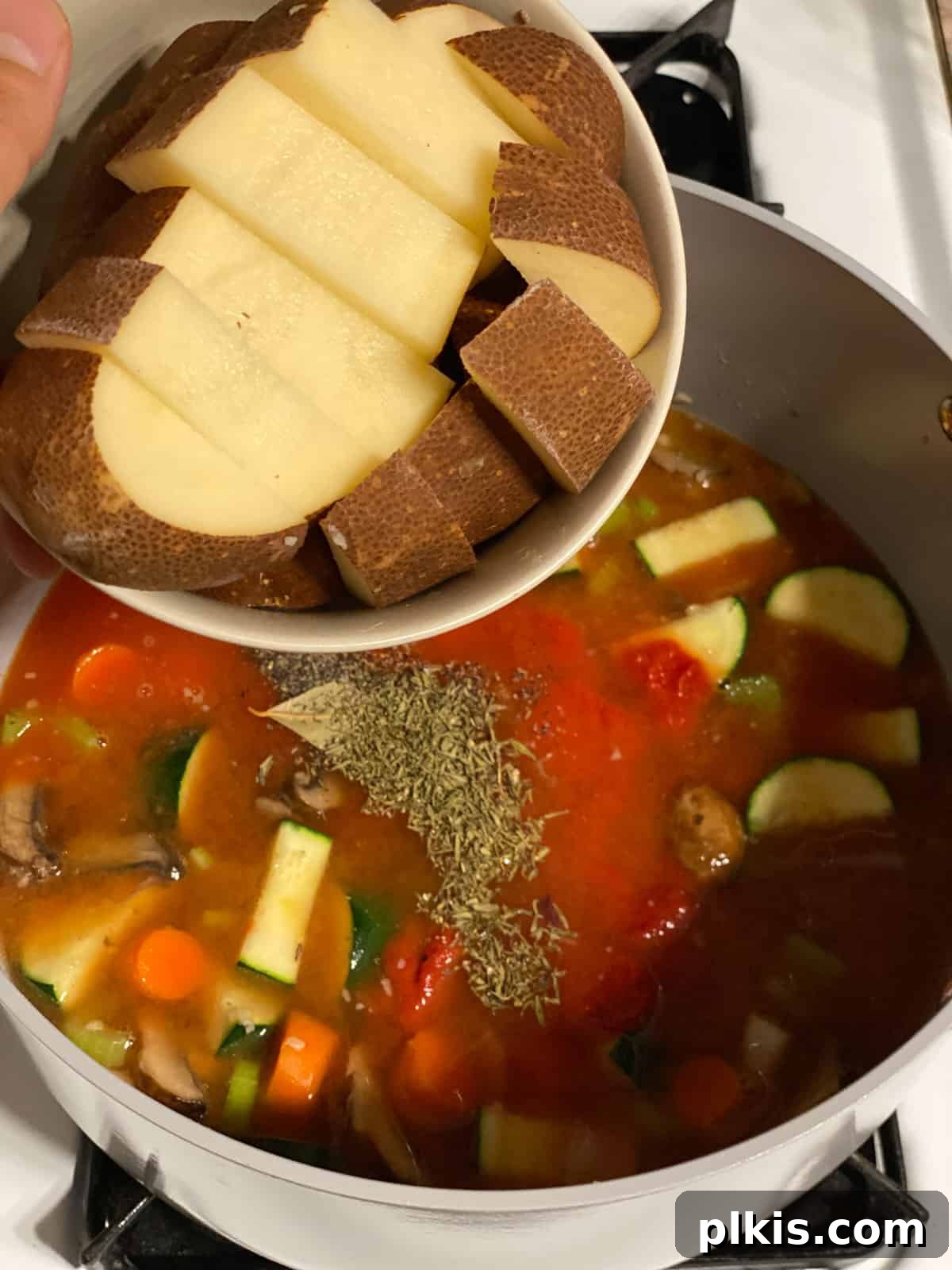 Hearty Tomato Potato Soup 14 Process shot of adding chopped potato to the soup mixture in the pot.