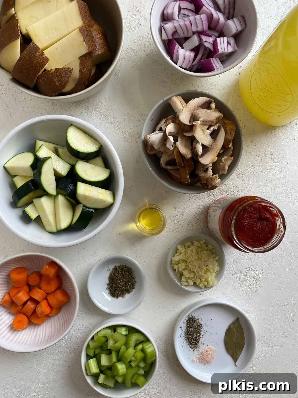 Hearty Tomato Potato Soup 3 A selection of fresh ingredients including onions, carrots, celery, zucchini, mushrooms, and potatoes laid out on a white surface, ready for making Tomato Soup with Potatoes.
