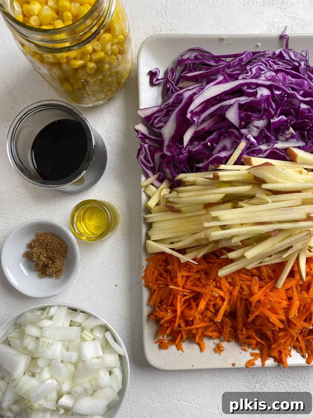 Garden Fresh Vegan Coleslaw with Apple, Carrots, and Corn 3 ingredients for slaw measured out and veggies cut on a white surface