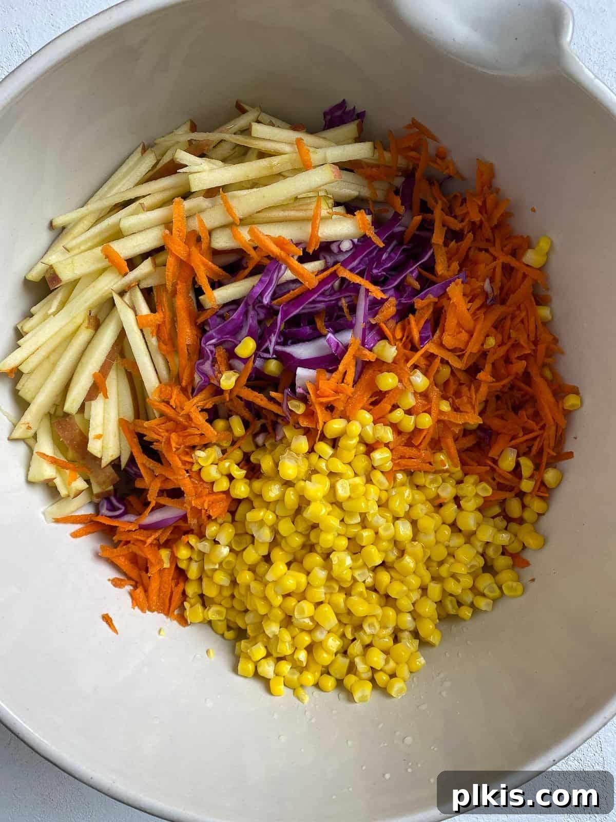 Garden Fresh Vegan Coleslaw with Apple, Carrots, and Corn 5 process of adding veggies for slaw into white bowl