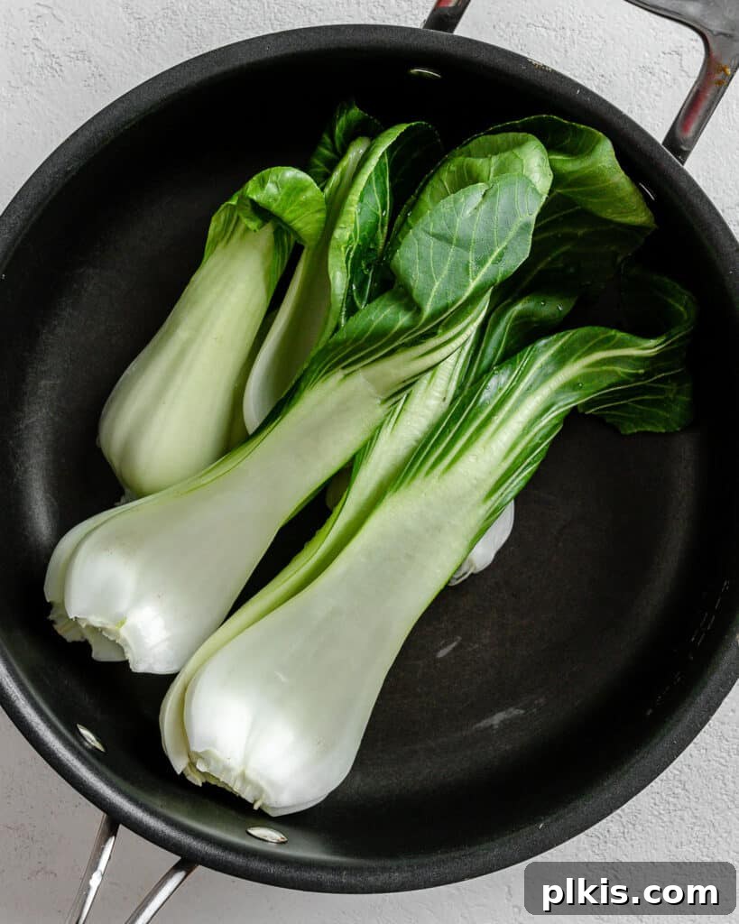 Savory Garlic Sesame Soba 5 Chopped yu choy (or another green vegetable) wilting in a black skillet, creating a vibrant contrast against a white background, signaling preparation for the noodle dish.
