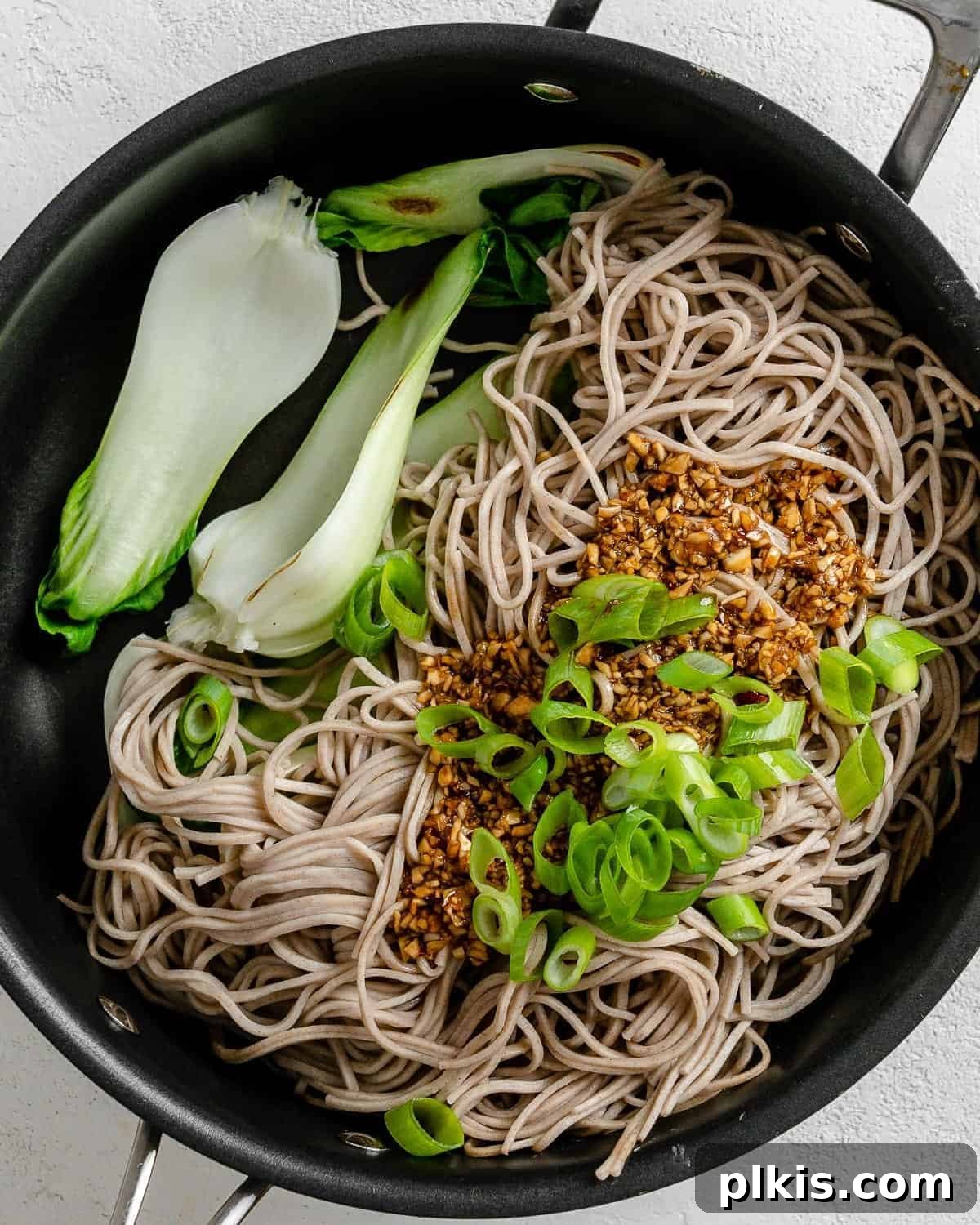 Savory Garlic Sesame Soba 7 A close-up view of the stir-fry process: soba noodles, green onions, and vegetables being tossed with the savory sesame sauce in a black pan, showcasing the harmonious blend of ingredients.