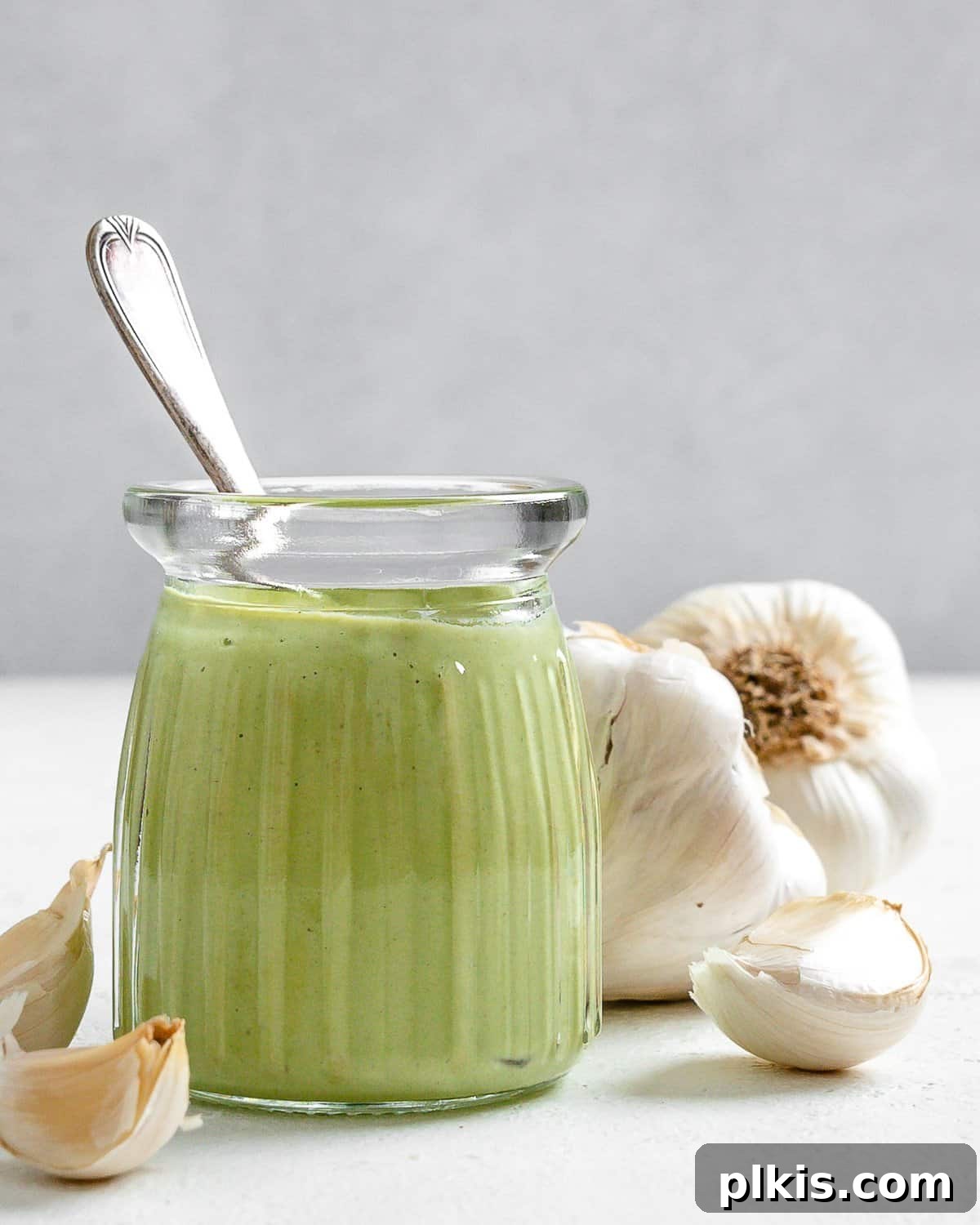 Completed Creamy Vegan Garlic Sauce in a glass jar with fresh garlic bulbs in the background, showcasing its rich and inviting texture.