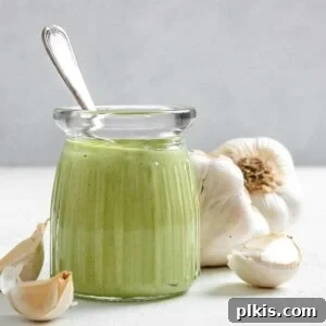 completed Creamy Vegan Garlic Sauce in a glass jar with garlic in the background