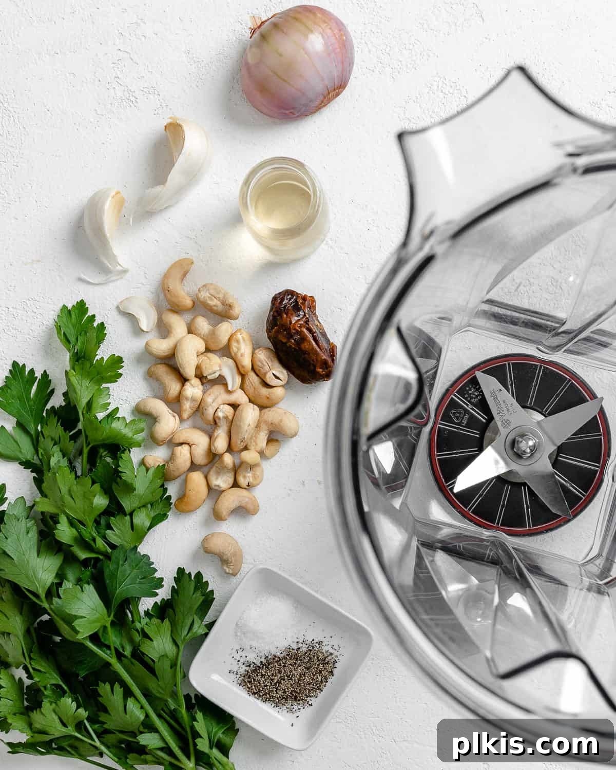 Ingredients for Creamy Vegan Garlic Sauce alongside a blender on a white background, ready for preparation.