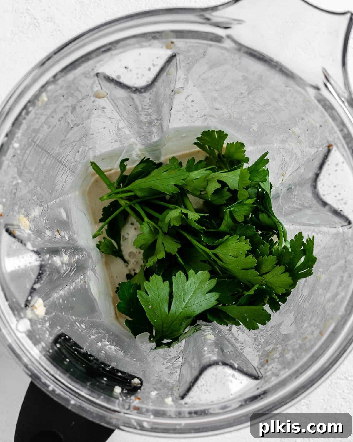 Process shot illustrating the addition of fresh cilantro into a blender containing Creamy Vegan Garlic Sauce, for an herbaceous finish.