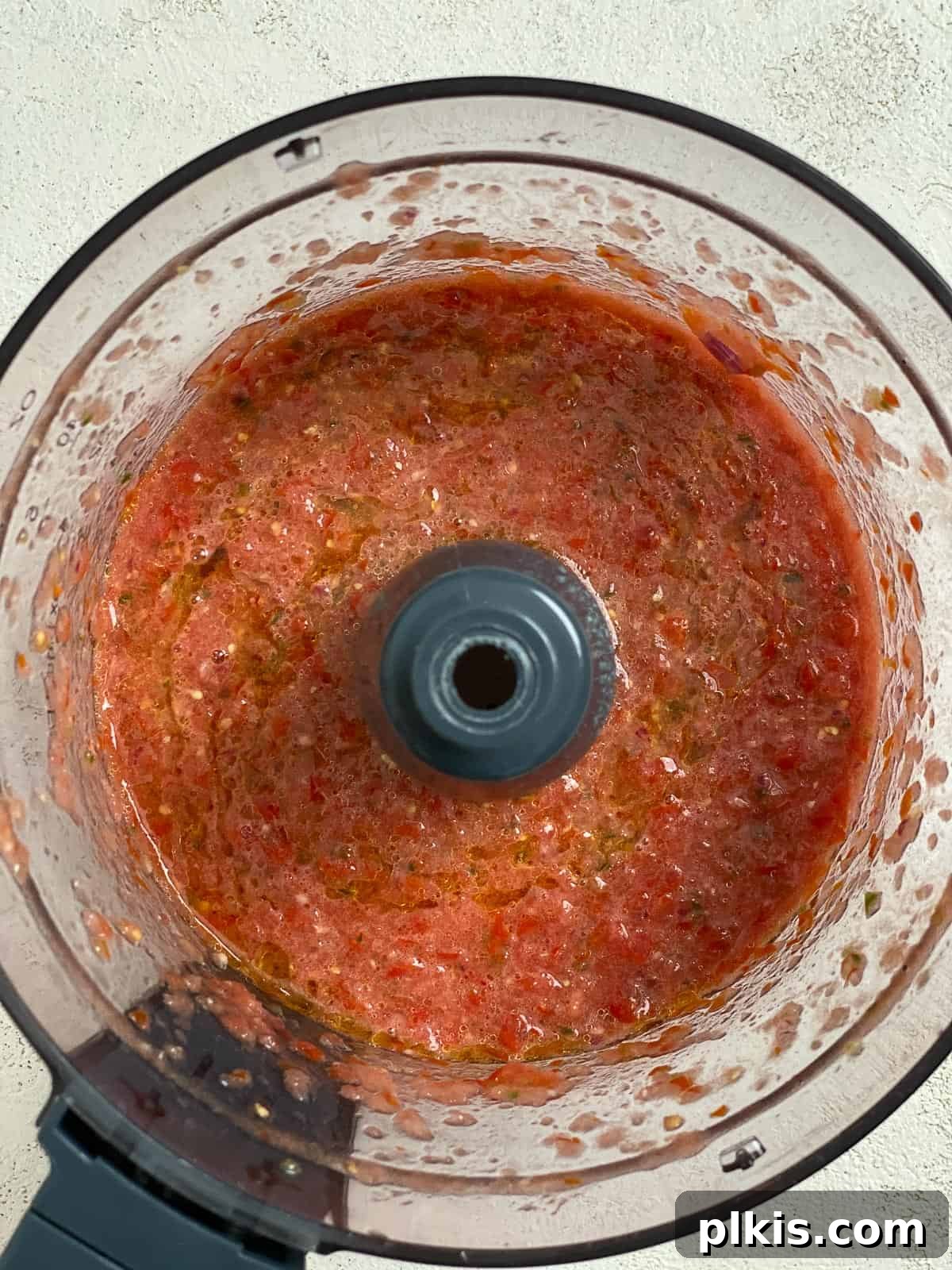 Blender Magic: 5-Minute Restaurant Salsa 6 The blended salsa ingredients inside the food processor, showing a smooth yet slightly textured consistency.