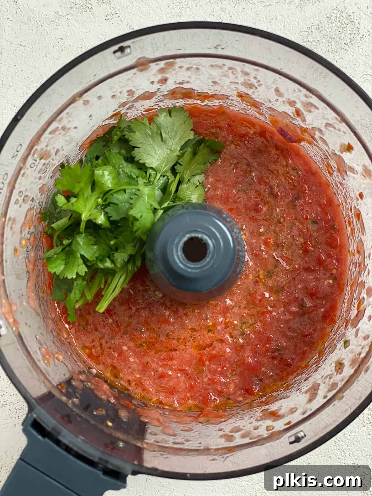 Blender Magic: 5-Minute Restaurant Salsa 7 Fresh cilantro leaves being added into the food processor with the blended salsa base.