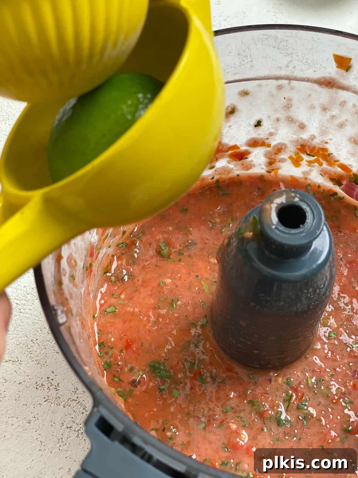 Blender Magic: 5-Minute Restaurant Salsa 9 A hand squeezing fresh lime juice directly into the food processor to season the salsa.