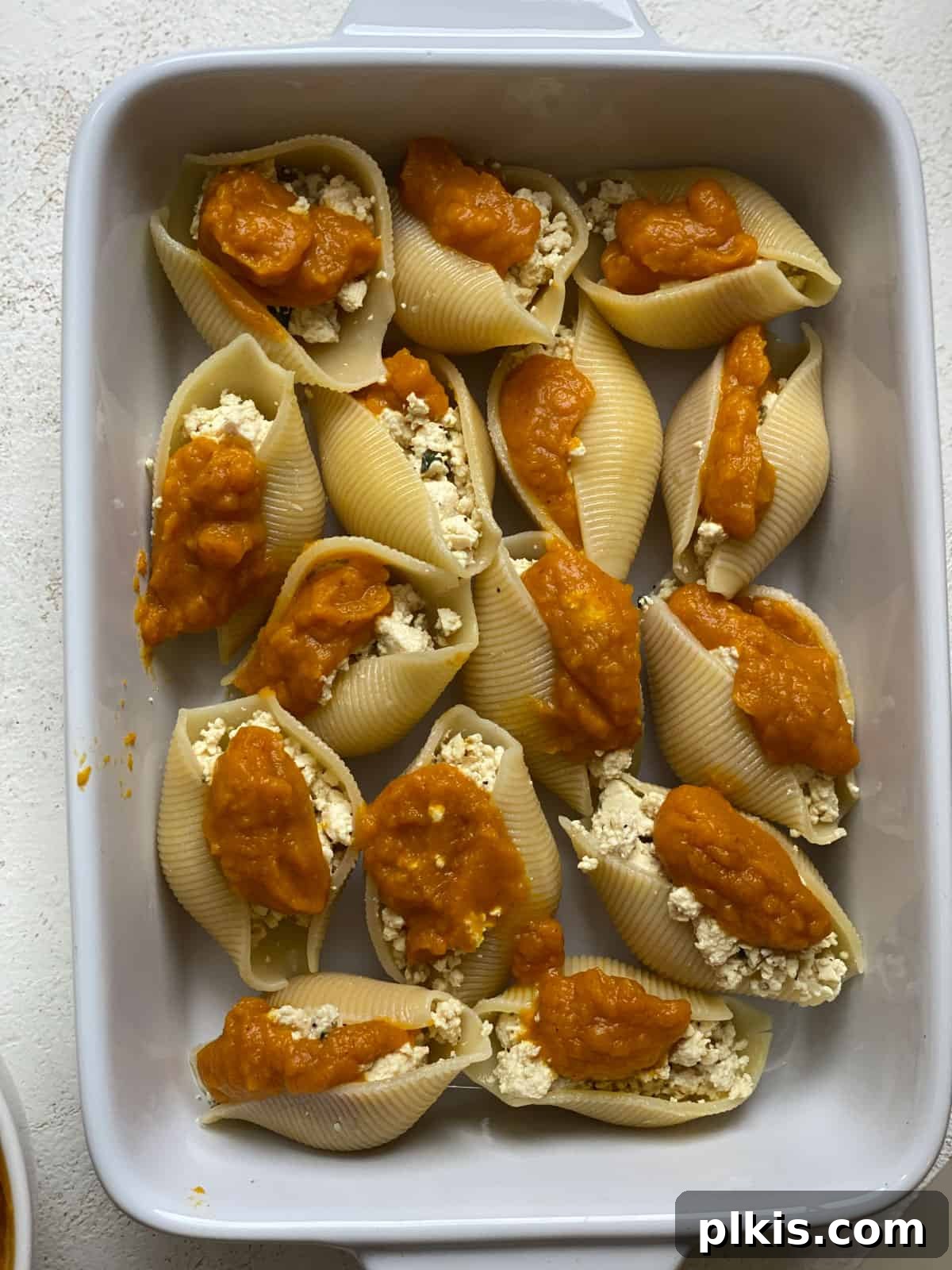 Autumn Pumpkin Pasta Shells with Aromatic Sage Cream 13 Several pumpkin stuffed shells arranged in a baking dish, ready for the oven