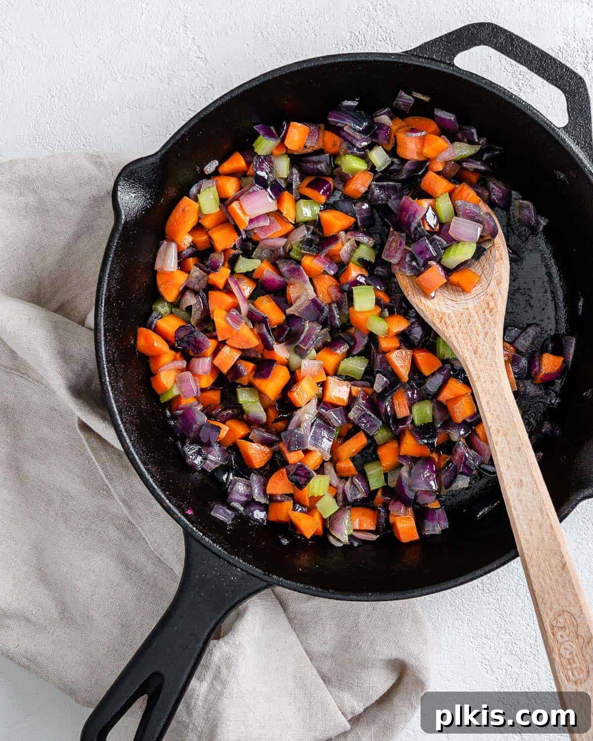 The Flavor Foundation 2 Perfectly cooked mirepoix in a black skillet with a wooden spoon, ready to be incorporated into a delicious dish.