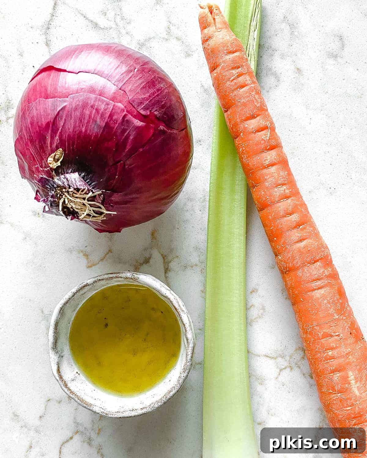 The Flavor Foundation 3 Freshly gathered ingredients for a delicious Mirepoix, including a yellow onion, carrots, and celery stalks, artfully arranged on a clean white surface.