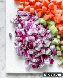 The Flavor Foundation 5 Uniformly diced mirepoix ingredients—carrots, celery, and onions—neatly arranged on a white cutting board, showcasing precise preparation.