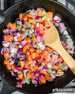 The Flavor Foundation 8 A wooden spoon stirring the mirepoix vegetables—carrots, celery, and onions—as they gently cook and soften in a black skillet.
