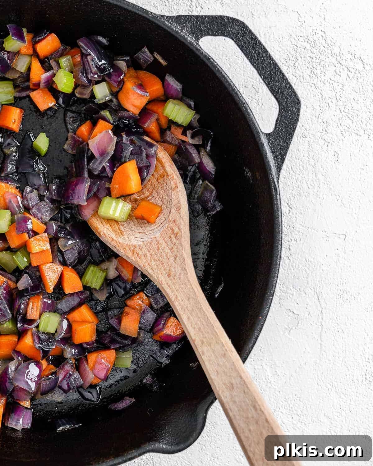 The Flavor Foundation 10 The finished Mirepoix, boasting tender, aromatic vegetables, is captured in a black skillet with a wooden spoon, ready for various culinary applications.