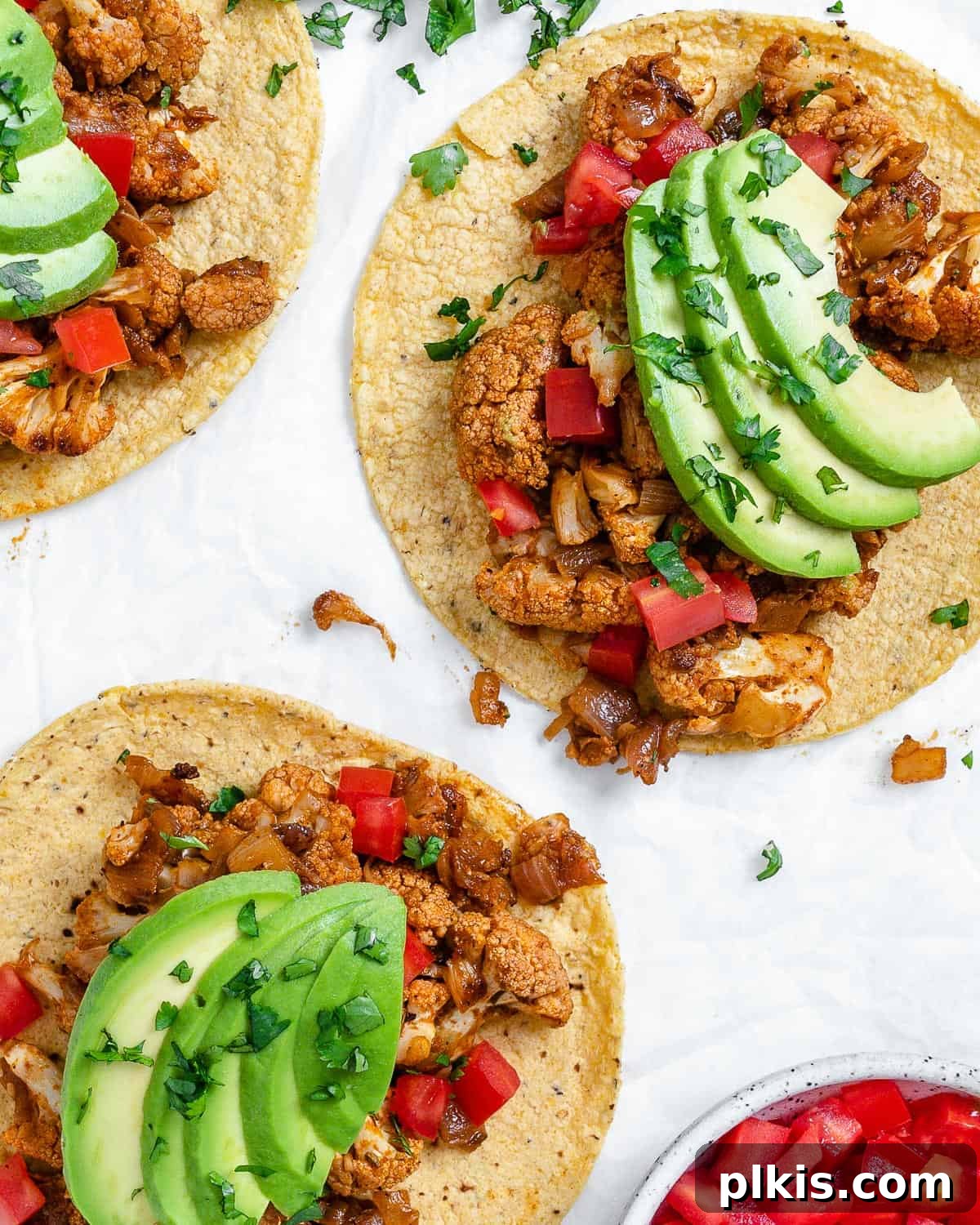Roasted Cauliflower Tacos 2 Delicious Cauliflower and Lentil Tacos generously topped with fresh ingredients, spread out on a clean white surface, highlighting their vibrant appeal.