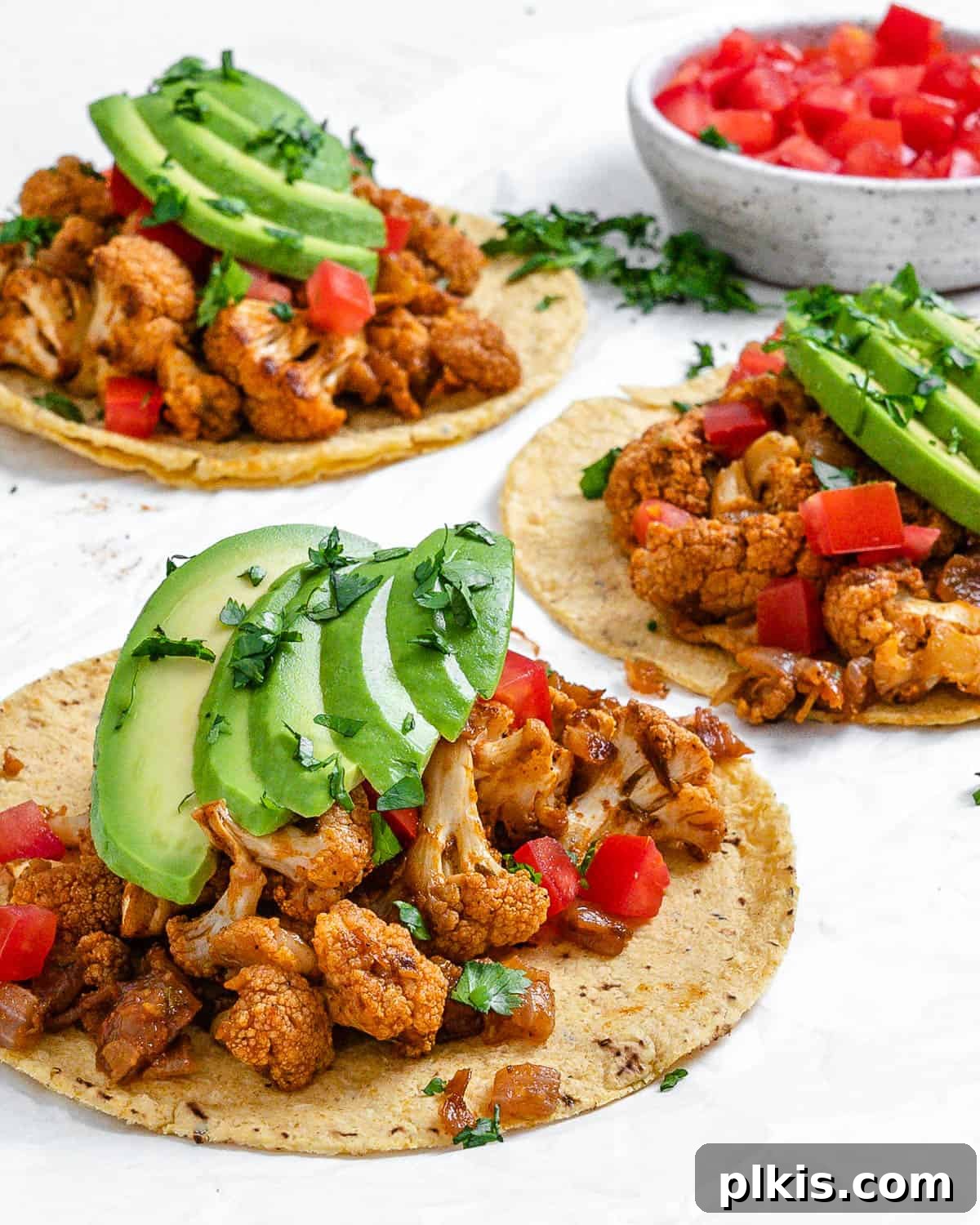 Roasted Cauliflower Tacos 12 A stunning overhead shot of perfectly assembled Cauliflower and Lentil Tacos, garnished with fresh cilantro and lime wedges, presented on a white surface.
