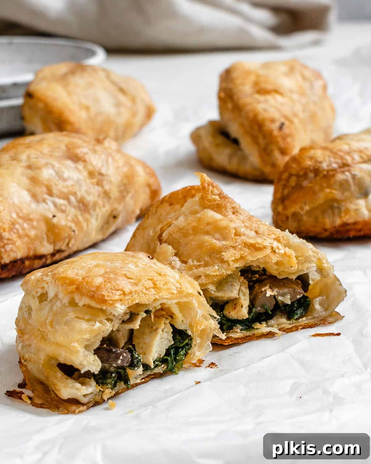 Several completed Spinach and Mushroom Puffs [Vegan Hand Pies] scattered on a white surface.
