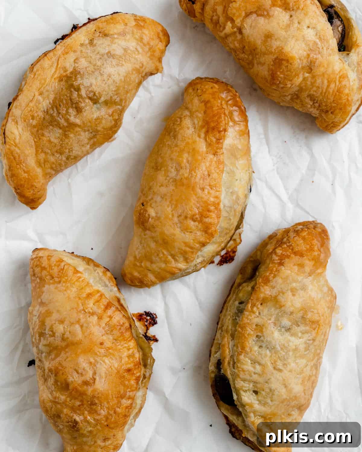 Several completed Spinach and Mushroom Puffs [Vegan Hand Pies] scattered on a white surface.