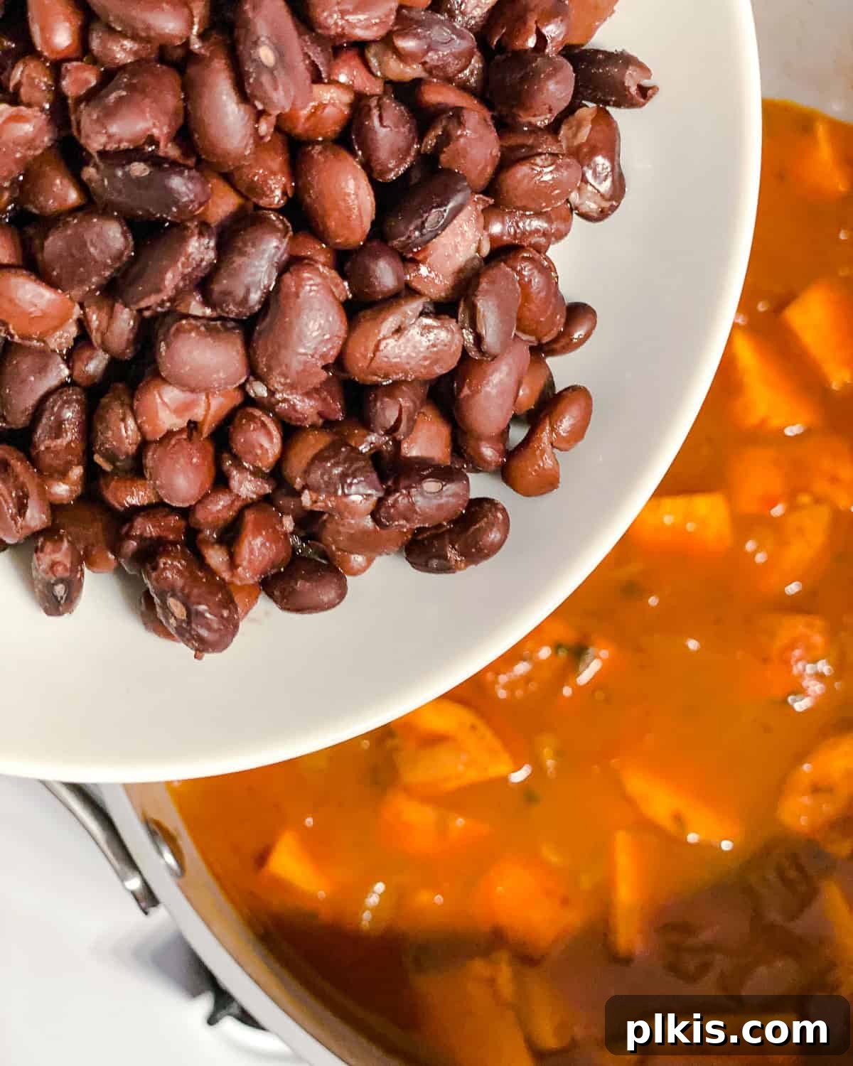 Hearty Sweet Potato Quinoa Chili 7 Process shot showing a can of drained and rinsed black beans being added to the simmering chili mixture, ready to meld with the other ingredients.