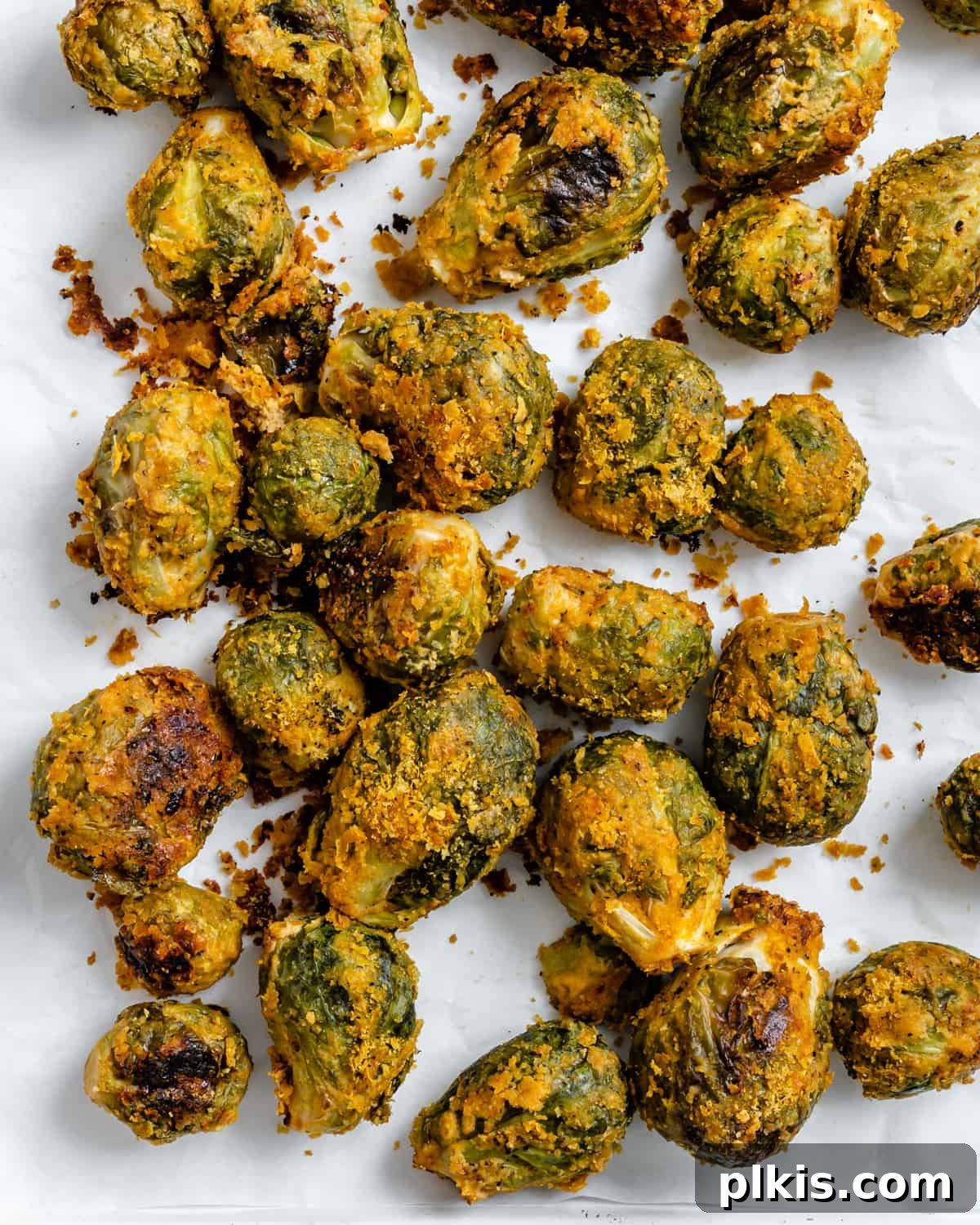 Effortless Vegan Brussels Sprouts Delight 2 Crispy, cheesy Easy Vegan Brussels Sprouts with Tahini scattered on a white surface, garnished with fresh herbs
