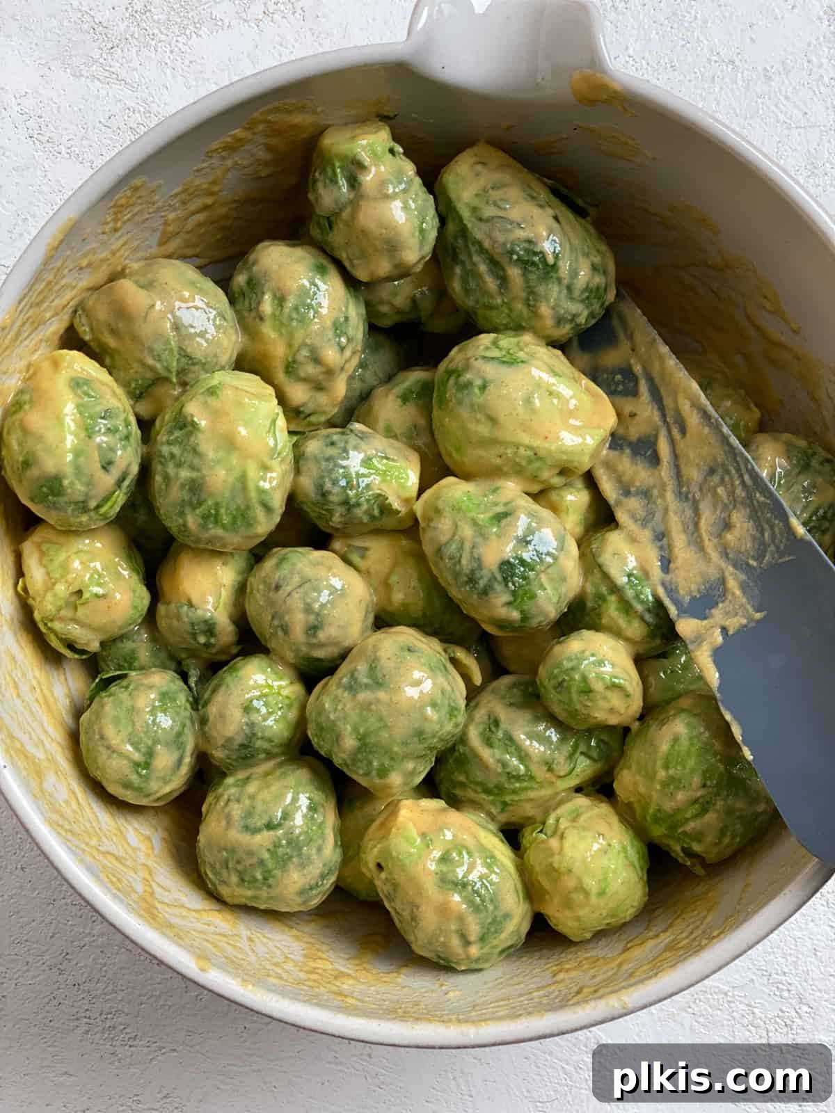 Effortless Vegan Brussels Sprouts Delight 8 Brussels sprouts being tossed with the creamy tahini sauce in a mixing bowl