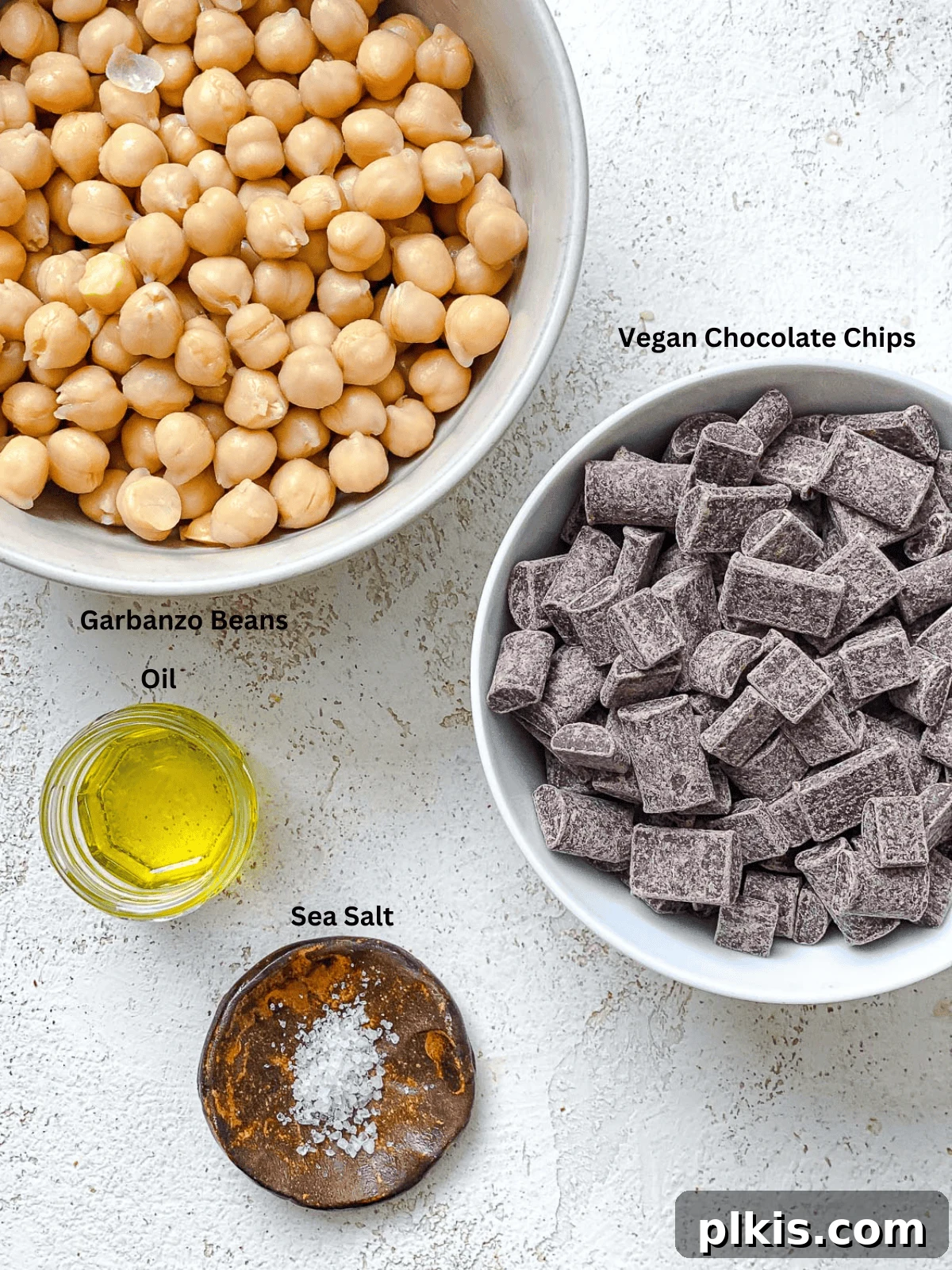 Irresistible Chocolate Chickpea Bites 3 Assortment of ingredients for chocolate covered chickpeas, including canned chickpeas, olive oil, sea salt, and vegan chocolate chips, neatly arranged on a white surface.