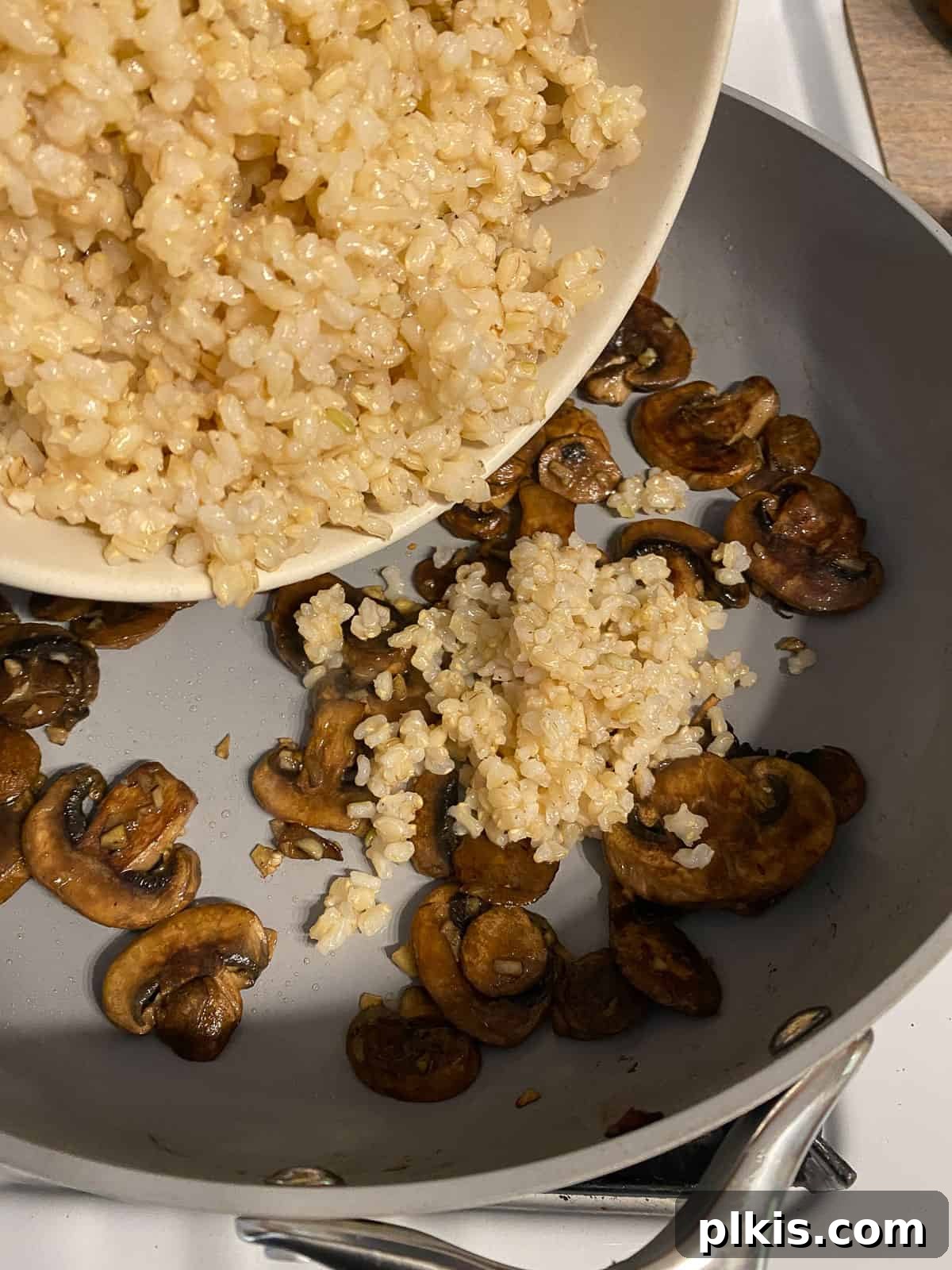 Velvety Brown Rice Risotto 8 Process shot of cooked brown rice being added to a pan with sautéed mushrooms.