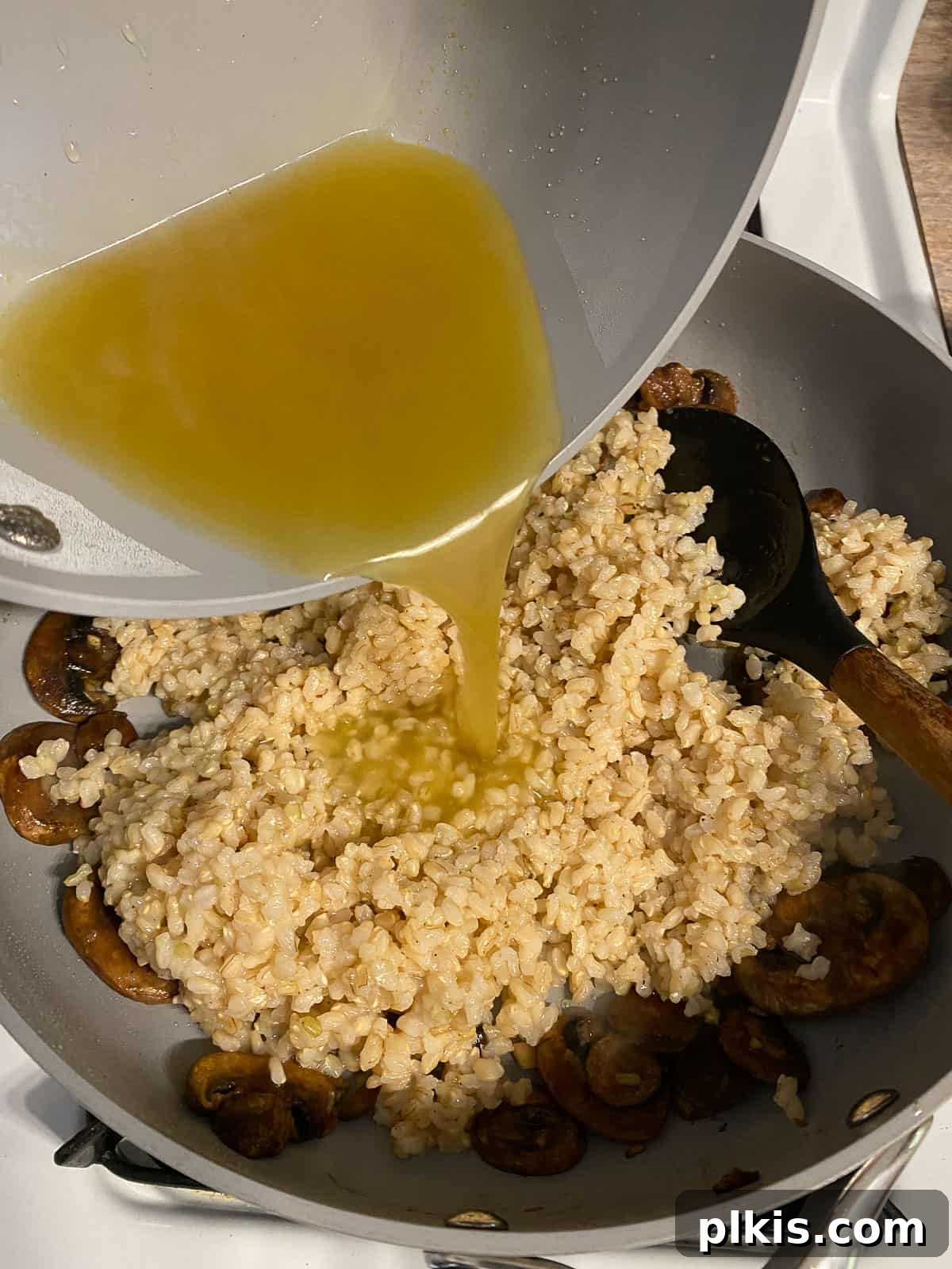 Velvety Brown Rice Risotto 9 Process shot of warmed vegetable broth being added to the pan with rice and mushrooms.