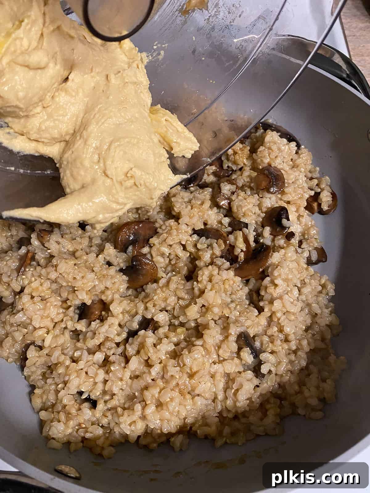 Velvety Brown Rice Risotto 10 Process shot of adding the white bean puree to the pan with rice and mushrooms.