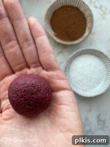 A perfectly rolled beet energy ball held in the palm of a hand, with ingredients blurred in the background, highlighting its vibrant color.