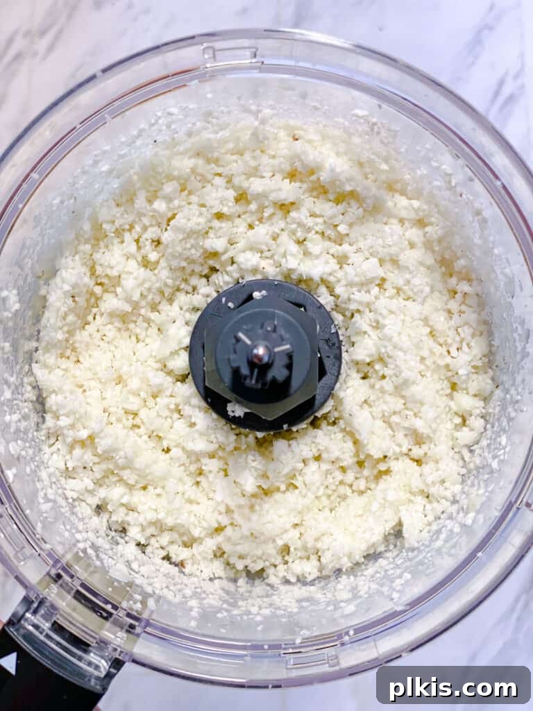 Nutrient-Packed Stuffed Avocado Delights 5 Close-up process shot of riced cauliflower inside a food processor bowl after processing.