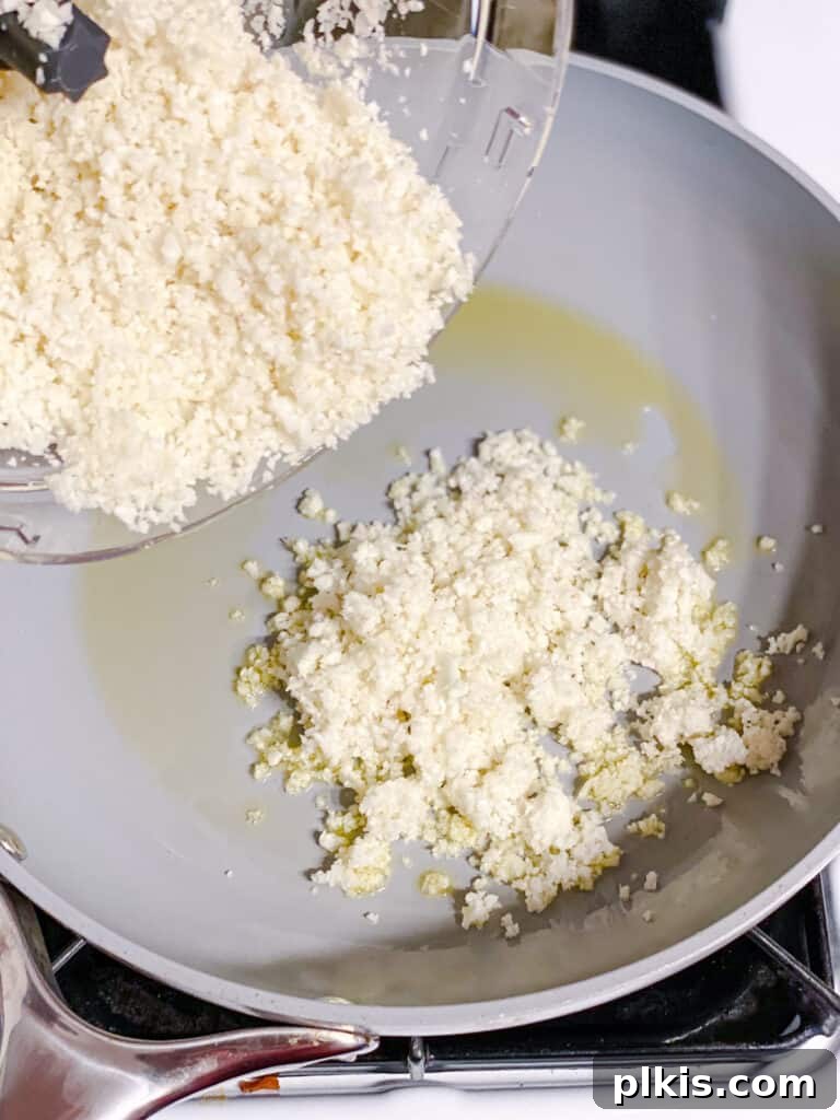 Nutrient-Packed Stuffed Avocado Delights 6 Process shot showing riced cauliflower being added to a hot skillet for sautéing.