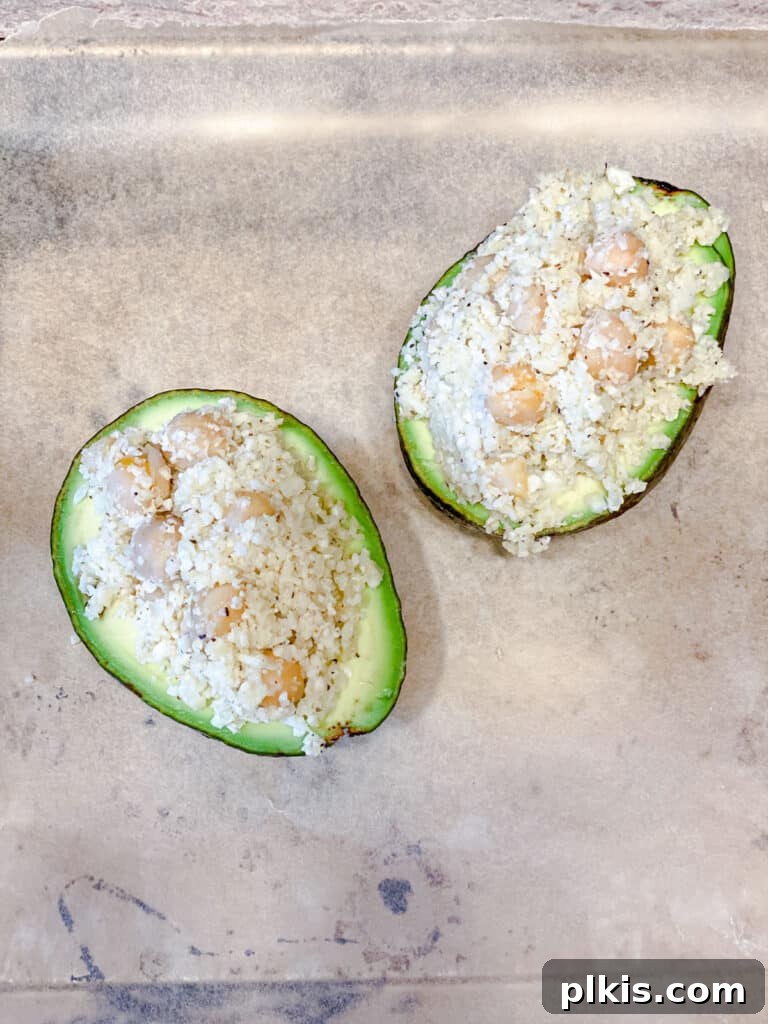 Nutrient-Packed Stuffed Avocado Delights 9 Process shot of the cauliflower and chickpea filling being spooned into avocado halves.