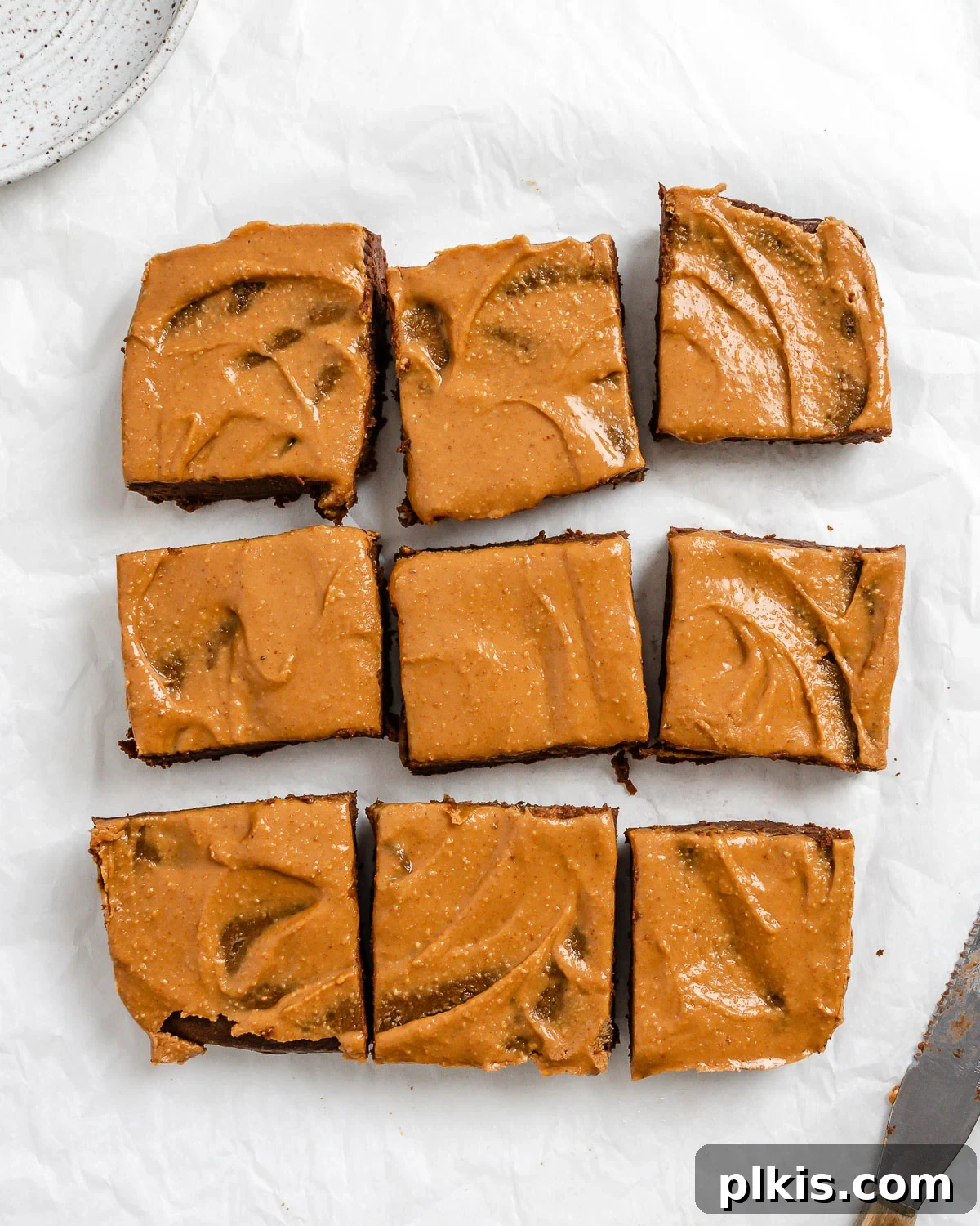 Decadent Vegan Sweet Potato Brownies 2 completed Sweet Potato Brownies cut into 9 squares on a white surface, topped with peanut butter