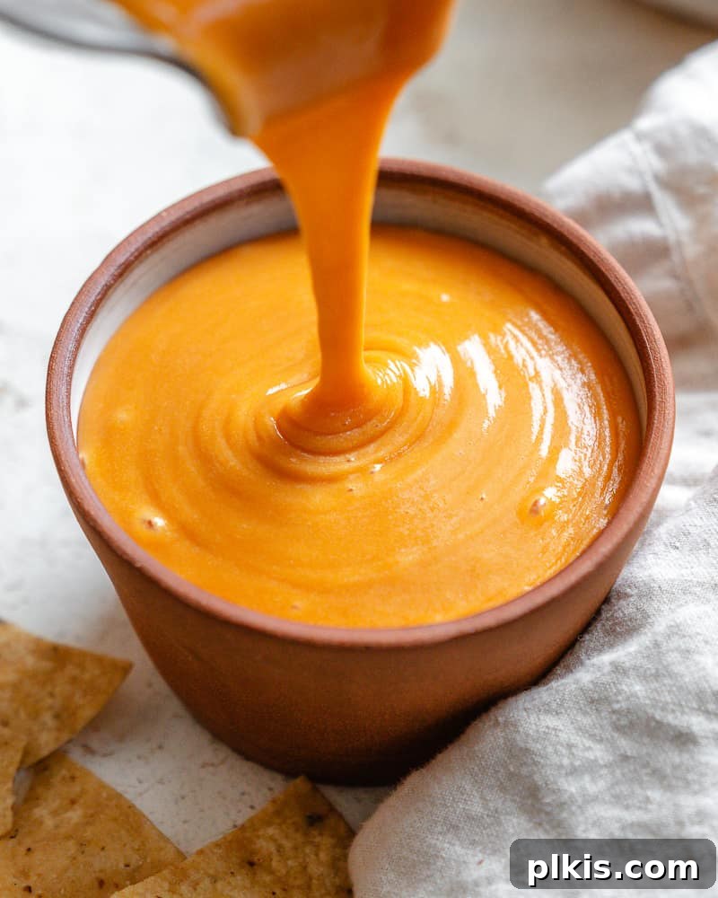 Rich Nacho Cheese Sauce 7 pouring rich, creamy vegan nacho cheese sauce into a small ceramic bowl for serving.