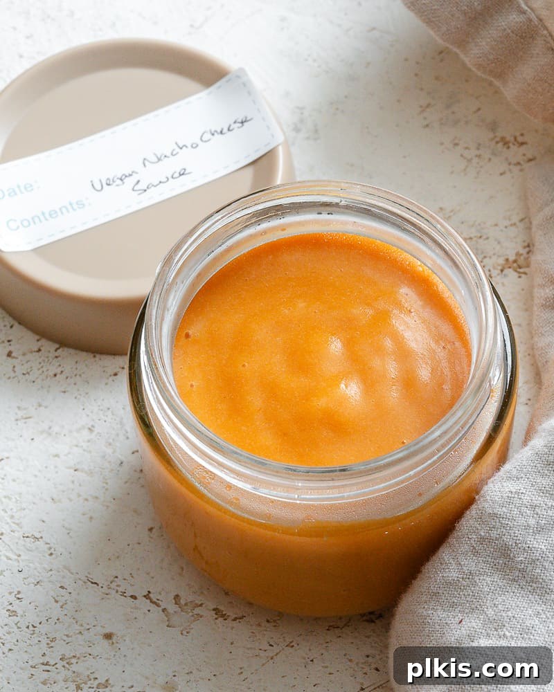 Rich Nacho Cheese Sauce 8 A clear glass jar filled with golden vegan nacho cheese sauce, with a label reading "Vegan Nacho Cheese Sauce" beside it, ready for storage.