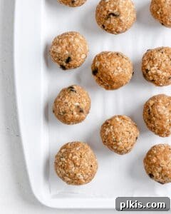 A tray lined with parchment paper holds several freshly rolled peanut butter oatmeal energy balls, neatly spaced and ready for freezing.