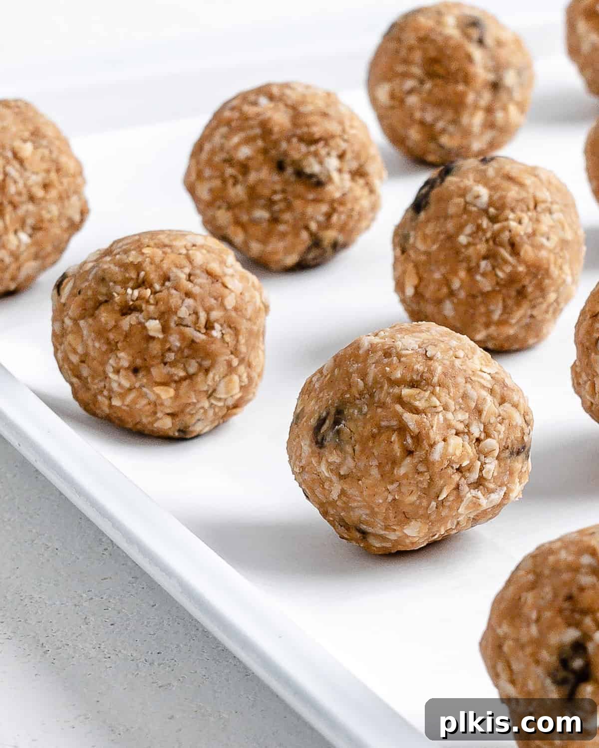 A close-up shot of several peanut butter oatmeal energy balls neatly arranged on a white tray, showcasing their perfectly round shape and inviting texture.